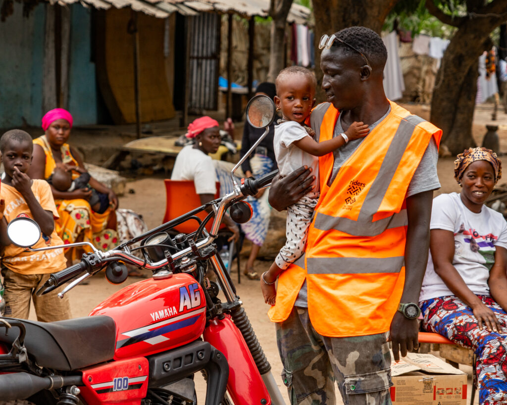 Man holding a child by a motorcycle in African village
